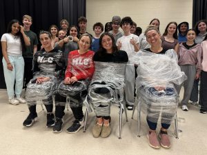 A group of students stand with their teachers who they've tied up with wrap after a community drive.