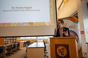 Medical Officer of Health Dr. Thomas Piggott speaks to a crowd at an event in a school library.