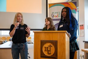 Two high school students stand with an adult at an event in a school library.