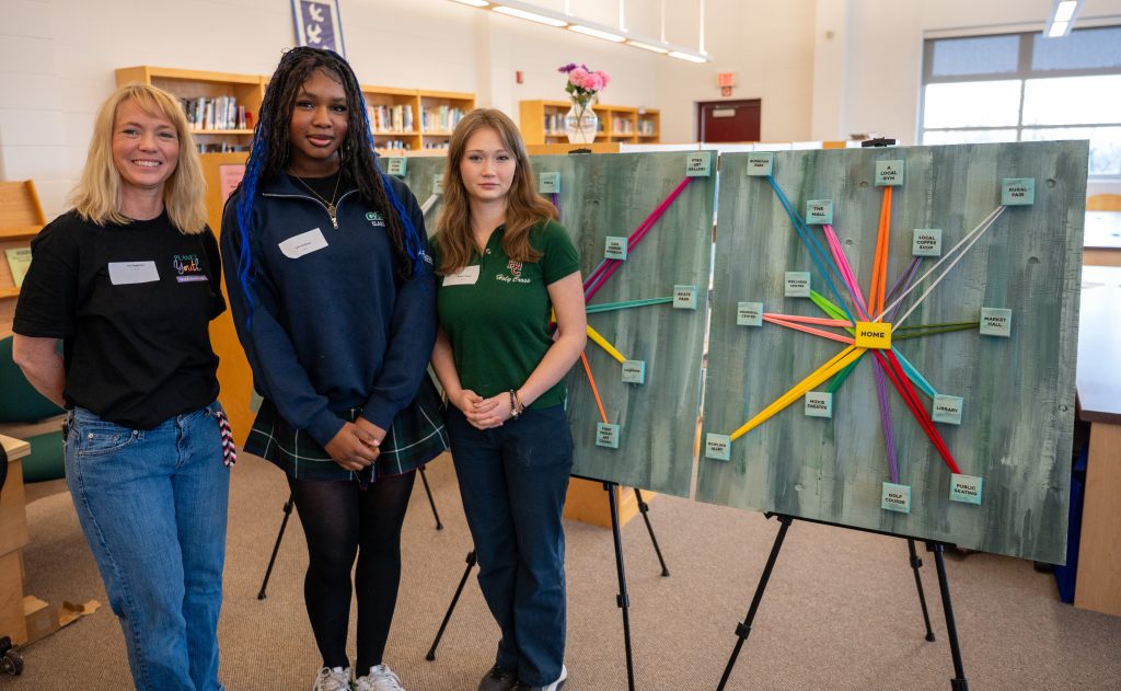 Two high school students stand with an adult in front of a new community art installation.