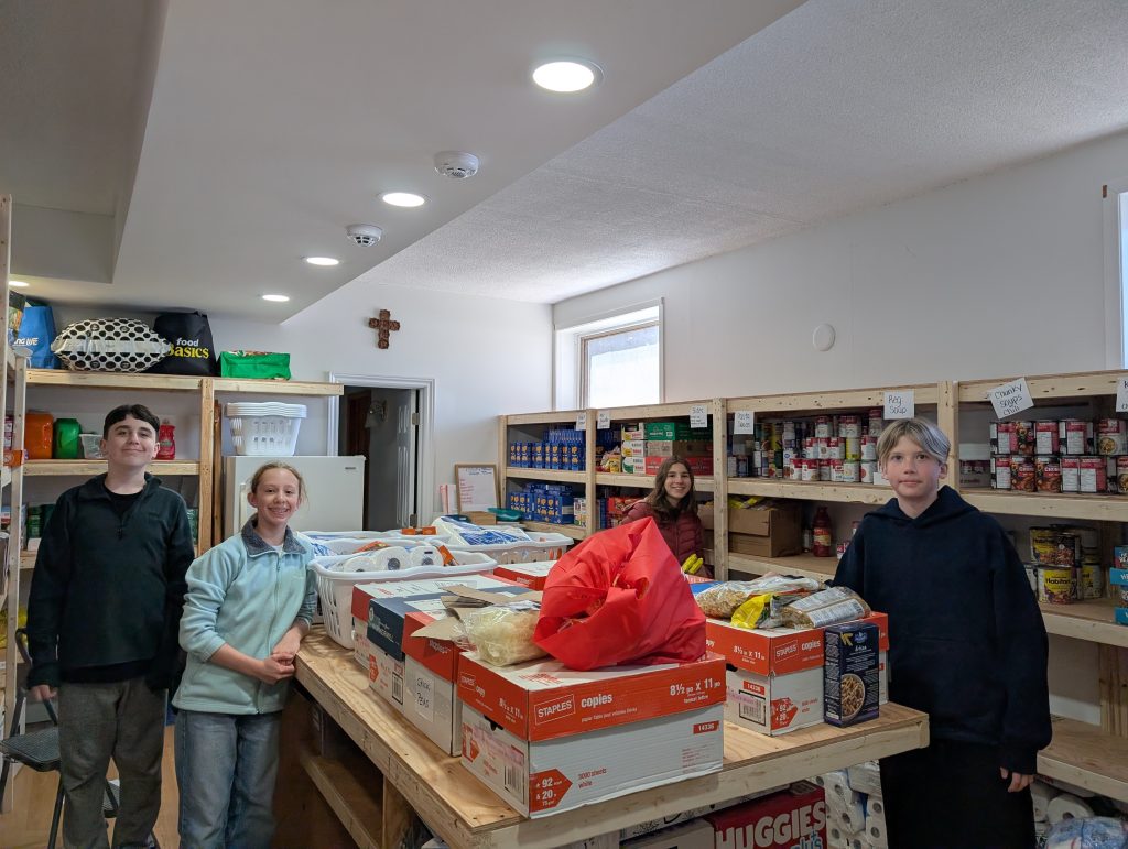 Four students stand in a food pantry at a church after collecting food during a community drive.