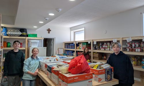 Four students stand in a food pantry at a church after collecting food during a community drive.