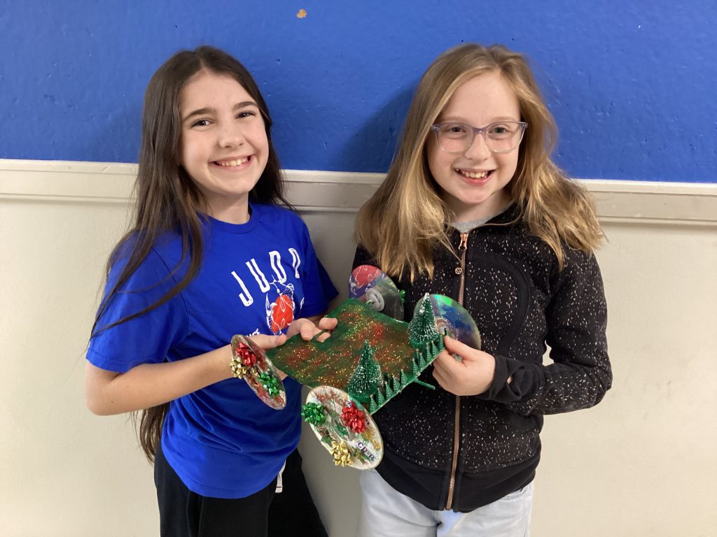 Two young female students stand with their junk drawer car creation which she used in a race.