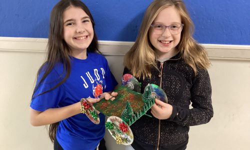 Two young female students stand with their junk drawer car creation which she used in a race.