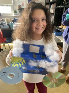 Young female student stands with her junk drawer car creation which she used in a race.