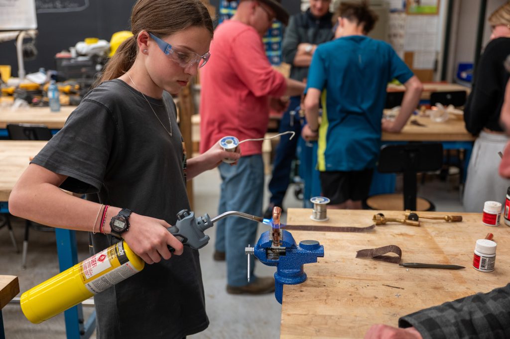 Young female student hold a torch as she welds a copper pipe.