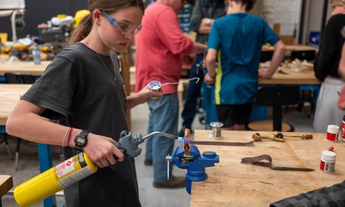 Young female student hold a torch as she welds a copper pipe.