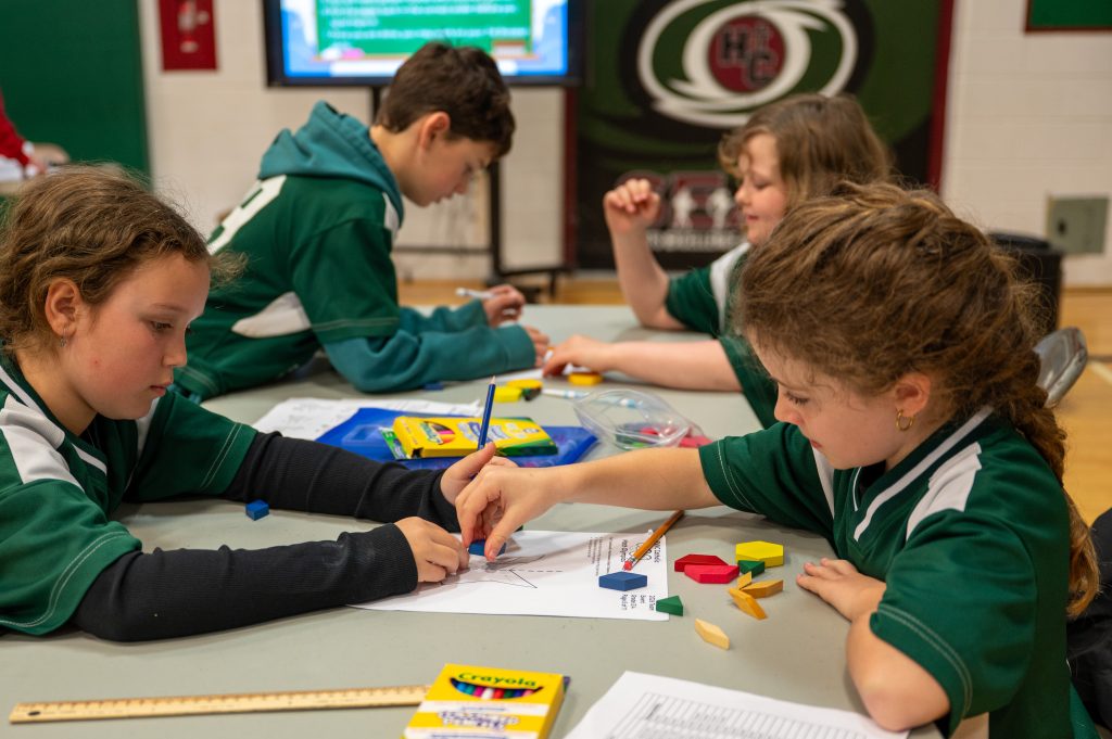 Four students wearing green work on math problems together at a competition in a school gym.