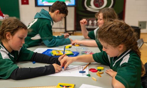 Four students wearing green work on math problems together at a competition in a school gym.