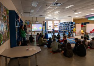 A group of elementary students gathers together in a school library for a meditation exercise.