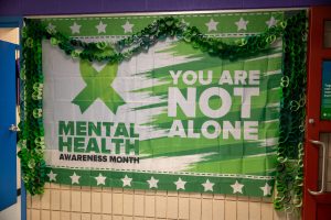 A green and white banner for Mental Health with the words "You are Not Alone" is displayed on a school hallway wall.