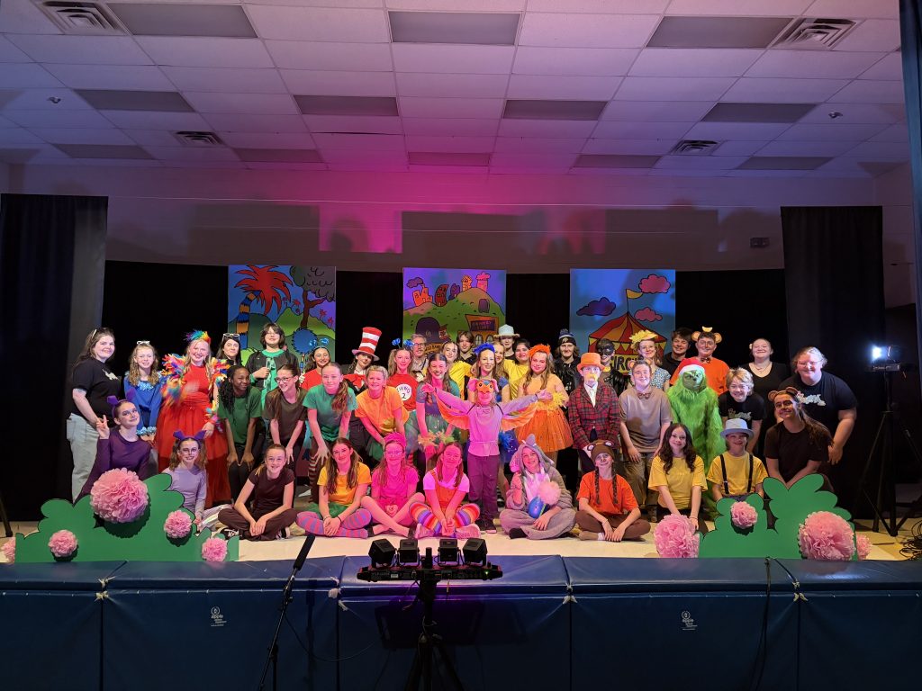 A large group of students wearing colourful costumes gather on stage for a musical.