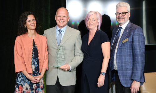 Four adults pose for a photo at an awards ceremony. The second person from the left, Alex Duketow, was named the Dick Hopkins Award recipient by Skills Ontario.