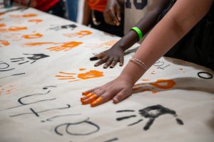 Secondary school students paint their hands orange and black and press them onto a banner for Indigenous History Month.