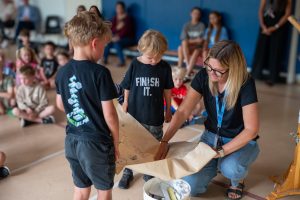 Two students and a teacher open a time capsule in a school gym.