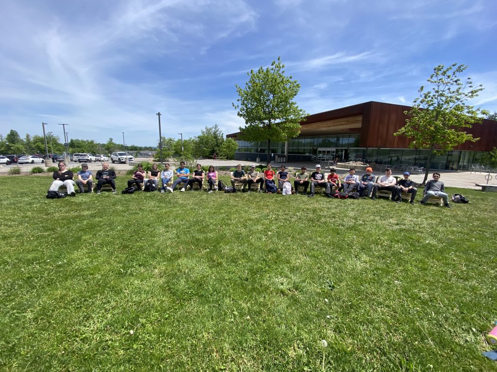 Twenty-one students sit in Muskoka chairs that they built at a college skilled trades day event.