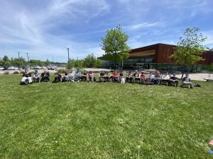 Twenty-one students sit in Muskoka chairs that they built at a college skilled trades day event.