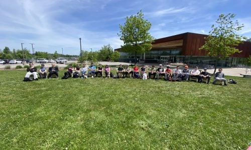 Twenty-one students sit in Muskoka chairs that they built at a college skilled trades day event.