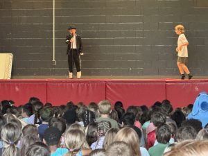 Two students perform a tribute to Michael Jackson on a stage in a school gymnasium in front of a crowd of students.