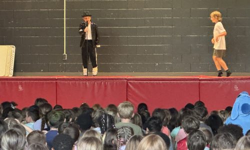 Two students perform a tribute to Michael Jackson on a stage in a school gymnasium in front of a crowd of students.