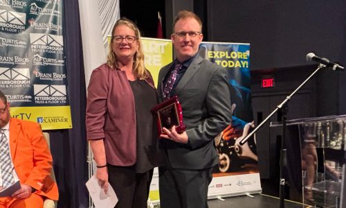 A man and woman stand on a stage holding an award at a ceremony.