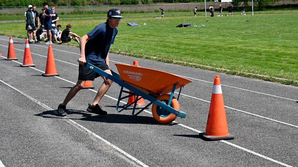 A student pushes a wheelbarrow through an obstacle course on a high school track.