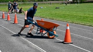 A student pushes a wheelbarrow through an obstacle course on a high school track.