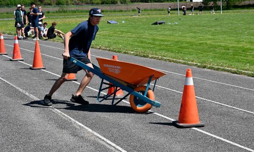 A student pushes a wheelbarrow through an obstacle course on a high school track.
