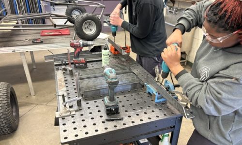 Two secondary school students use drills to fasten metal together for outdoor benches.
