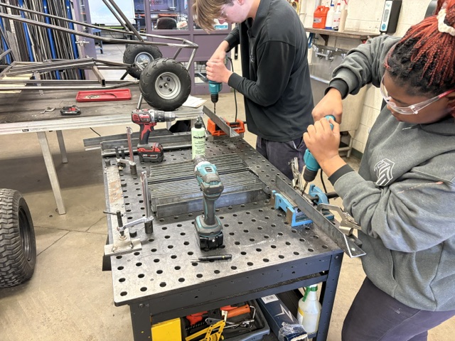 Two secondary school students use drills to fasten metal together for outdoor benches.